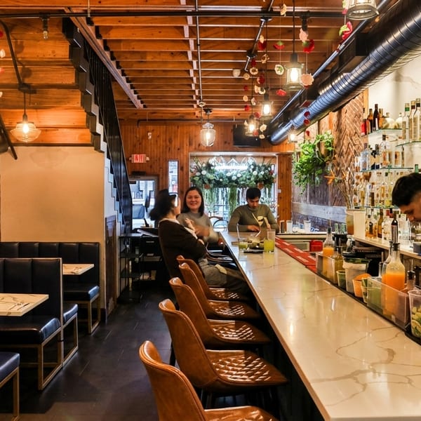 A cozy restaurant interior with a long bar, patrons, a bartender, and booth seating.