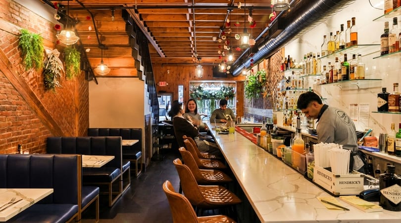 A cozy restaurant interior with a long bar, patrons, a bartender, and booth seating.