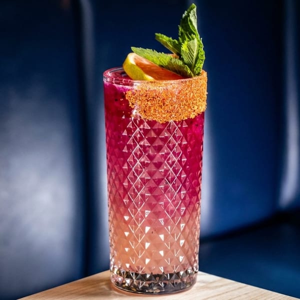 Pink cocktail in a textured glass with a spiced rim, grapefruit, and mint garnish.