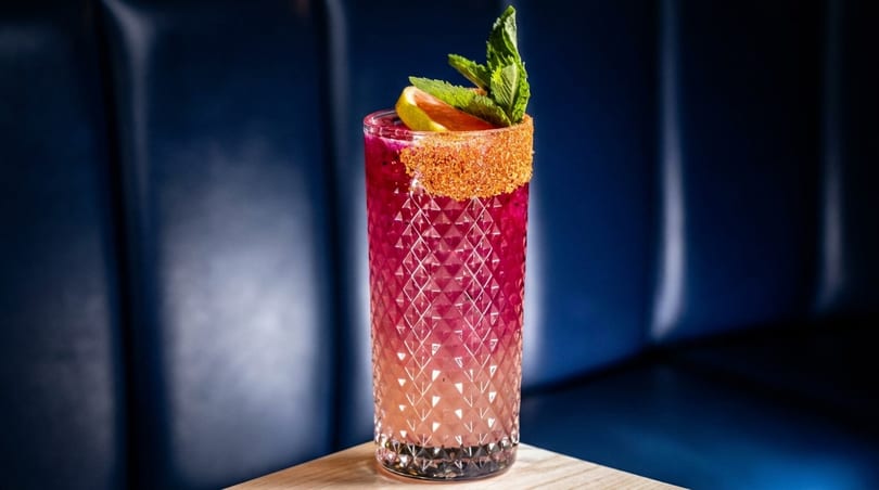 Pink cocktail in a textured glass with a spiced rim, grapefruit, and mint garnish.