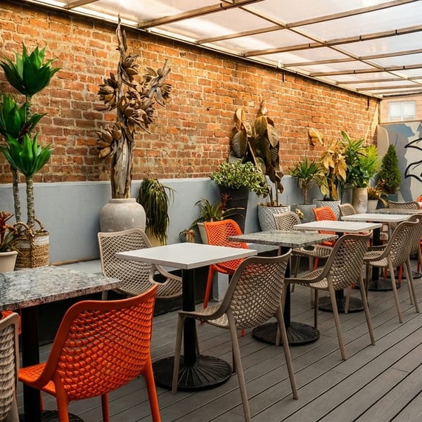 Outdoor patio with brick walls, potted plants, orange and beige chairs, and a pineapple mural.