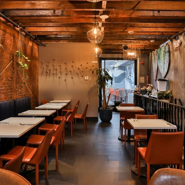 Restaurant interior with wooden walls, blue booth seating, orange chairs, and modern light fixtures.