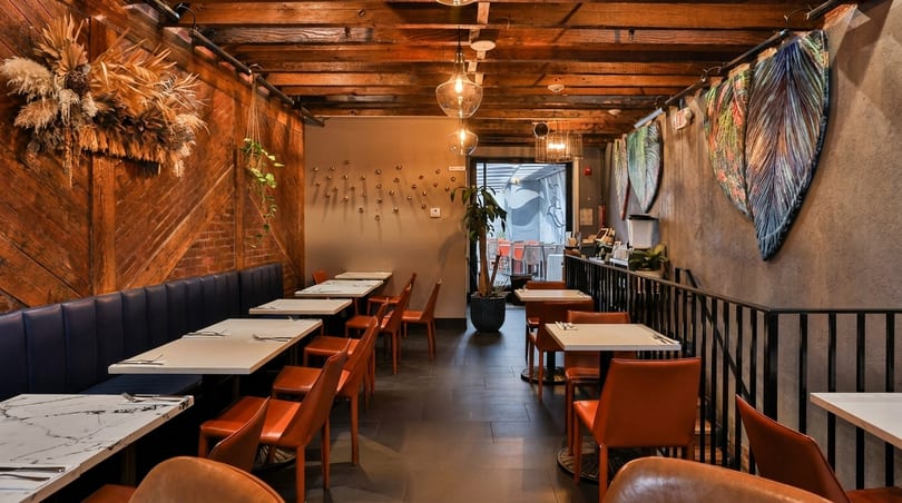 Restaurant interior with wooden walls, blue booth seating, orange chairs, and modern light fixtures.