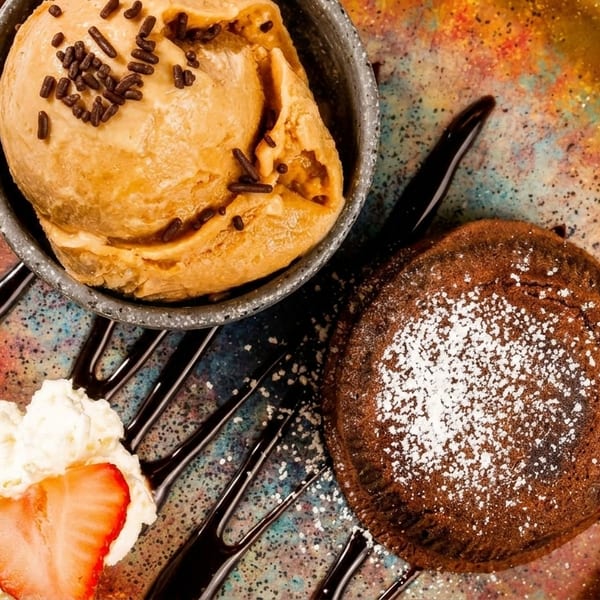 Chocolate lava cake with powdered sugar, a scoop of ice cream, whipped cream, and a strawberry.
