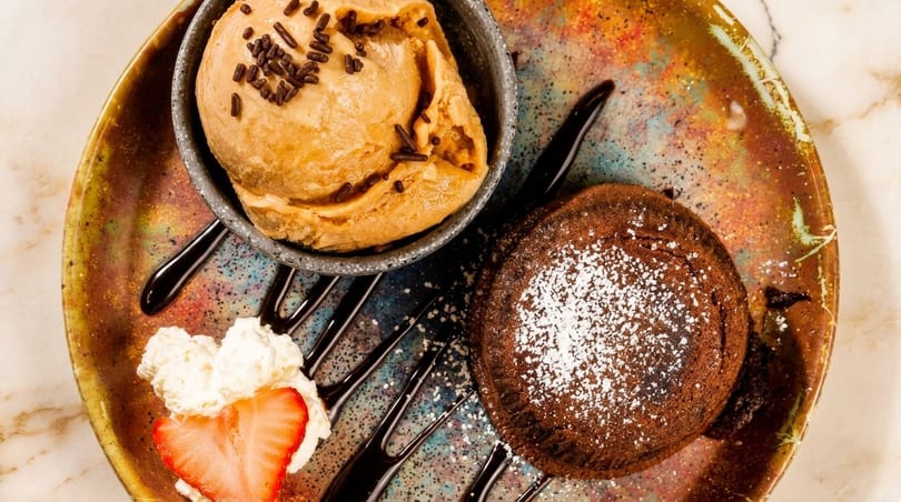 Chocolate lava cake with powdered sugar, a scoop of ice cream, whipped cream, and a strawberry.